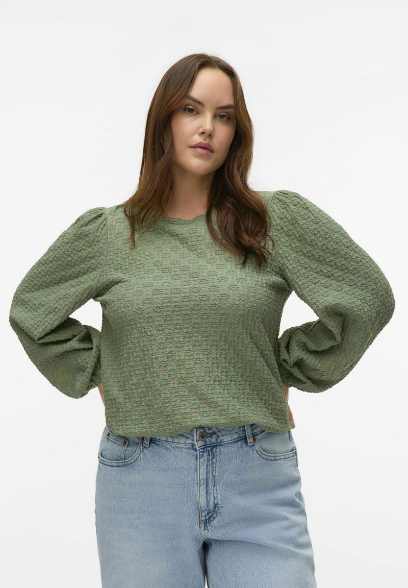 Top verde con texture, maniche lunghe a sbuffo, scollatura rotonda e vestibilità comoda, abbinato a jeans in denim blu chiaro.