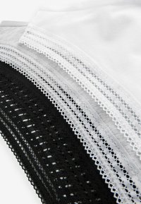 Set med tre tygstycken: svart, vitt och grått bomullsblandning. Varje bit har en delikat spetskant längs den övre kanten. Slät textur.