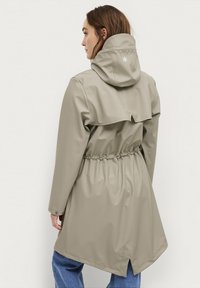 Lichtbeige waterdichte jas met een getailleerde taille, verstelbare capuchon en achterventilatie. Kenmerkt zich door een subtiele logo-detail op de capuchon.