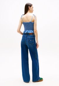 Lyseblå smocket crop top med volangkant og knyttebånd, kombinert med høyhalset, vide blå jeans med baklommer.