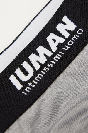 Close-up van een zwart-witte tailleband op grijs stof met de tekst "IUNAN" en "intimamente uomo" gebreid in het wit.