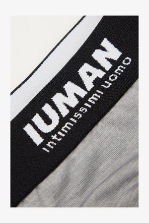 Close-up van een zwart-witte tailleband op grijs stof met de tekst "IUNAN" en "intimamente uomo" gebreid in het wit.