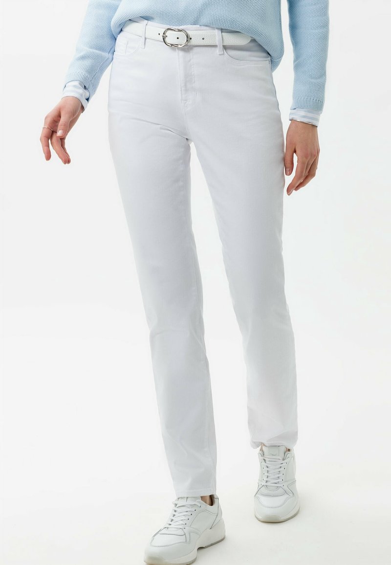Pantalones de algodón blancos de pierna recta, con tejido texturizado, combinados con un cinturón blanco con hebilla metálica, usados con zapatillas blancas.