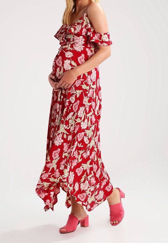 Rode maxi-jurk met bloemenprint en ruches aan de mouwen, voorzien van roze en witte bloemmotieven; gecombineerd met roze sandalen met blokhak.