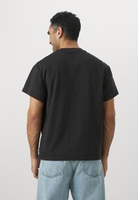 Sort bomulds T-shirt med korte ærmer, løs pasform og ren halsudskæring, parret med lyseblå denimjeans. Ensfarvet bagdesign uden grafik.