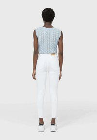 Top sin mangas de punto azul claro con patrón de trenzas, combinado con jeans skinny blancos de cintura alta y zapatillas blancas.