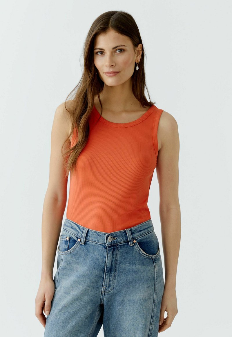 Geribbelde oranje tanktop met een brede halslijn, gecombineerd met hooggewaisted lichtblauwe jeans met voorzakken en een knoopsluiting.
