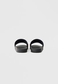 Czarne klapki na płaskiej, gładkiej gumowej podeszwie, z otwartym noskiem i szerokimi, zaokrąglonymi paskami dla wsparcia. Teksturowana powierzchnia zapewniająca przyczepność.