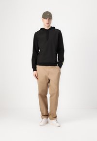 Hanorac negru cu siret, pantaloni bej și adidași albi, asortați cu o șapcă verde măsliniu. Design simplu, croială casual și detalii minime.