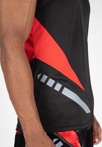 Schwarzes, athletisches Tank-Top mit roten und grauen geometrischen Mustern, aus glattem Material gefertigt und mit einer figurschmeichelnden Silhouette.