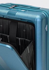 Hartschalenkoffer in metallischem Teal, mit geraffter Außenseite, doppeltem Reißverschluss und einem geräumigen schwarzen Innenraum mit Organisationsfächern.