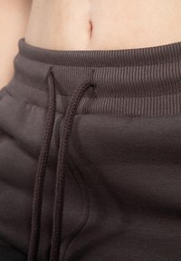 Nahaufnahme des Oberkörpers einer Person, die nackte Haut und braune, gerippte Sweatpants mit Kordelzug zeigt.