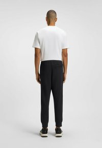 White short-sleeve t-shirt and black elastic-waist joggers with tapered legs, featuring a back pocket and ribbed cuffs. Sneakers complete the look.