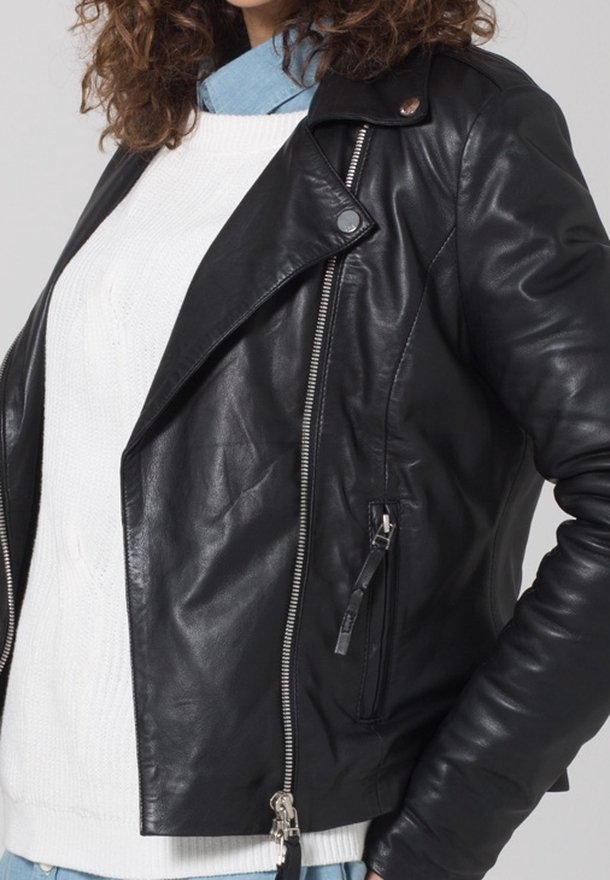 Femme portant une veste en cuir noire sur un pull en maille torsadée blanc et une chemise bleu clair à col, vue de la poitrine jusqu'aux hanches.