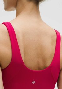 Fitted pink tank top with wide straps, a rounded back, and a small logo detail. Smooth texture and athletic design.