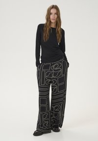 Schwarzes Langarmoberteil mit einer figurbetonten Silhouette, kombiniert mit lockeren schwarzen Hosen, die cremefarbene abstrakte Muster und seitliche Taschen aufweisen.