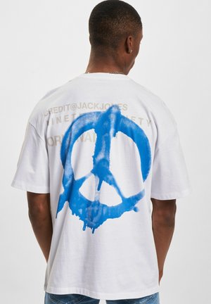 White cotton t-shirt featuring a large blue peace sign graphic on the back, with light beige text above it. Short sleeves and a relaxed fit.
