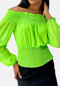 Jasnozielony top z odkrytymi ramionami, długimi przezroczystymi rękawami, marszczoną górą i falbaną przy dekolcie. Połączony z czarnym dopasowanym dołem.