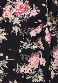 Robe noire à fleurs avec de grandes fleurs roses et blanches, ceinture nouée à la taille et fermeture par boutons. Tissu doux avec une texture légère.