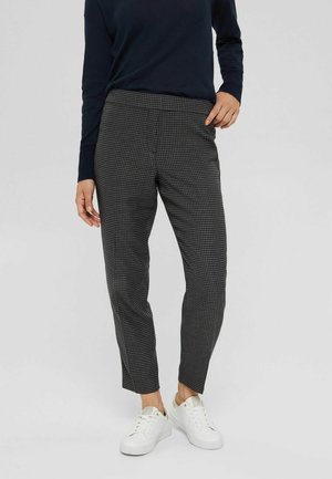 Pantalons à carreaux noirs et blancs avec une coupe ajustée, jambes fuselées, taille élastique et poches latérales, accompagnés de baskets blanches.