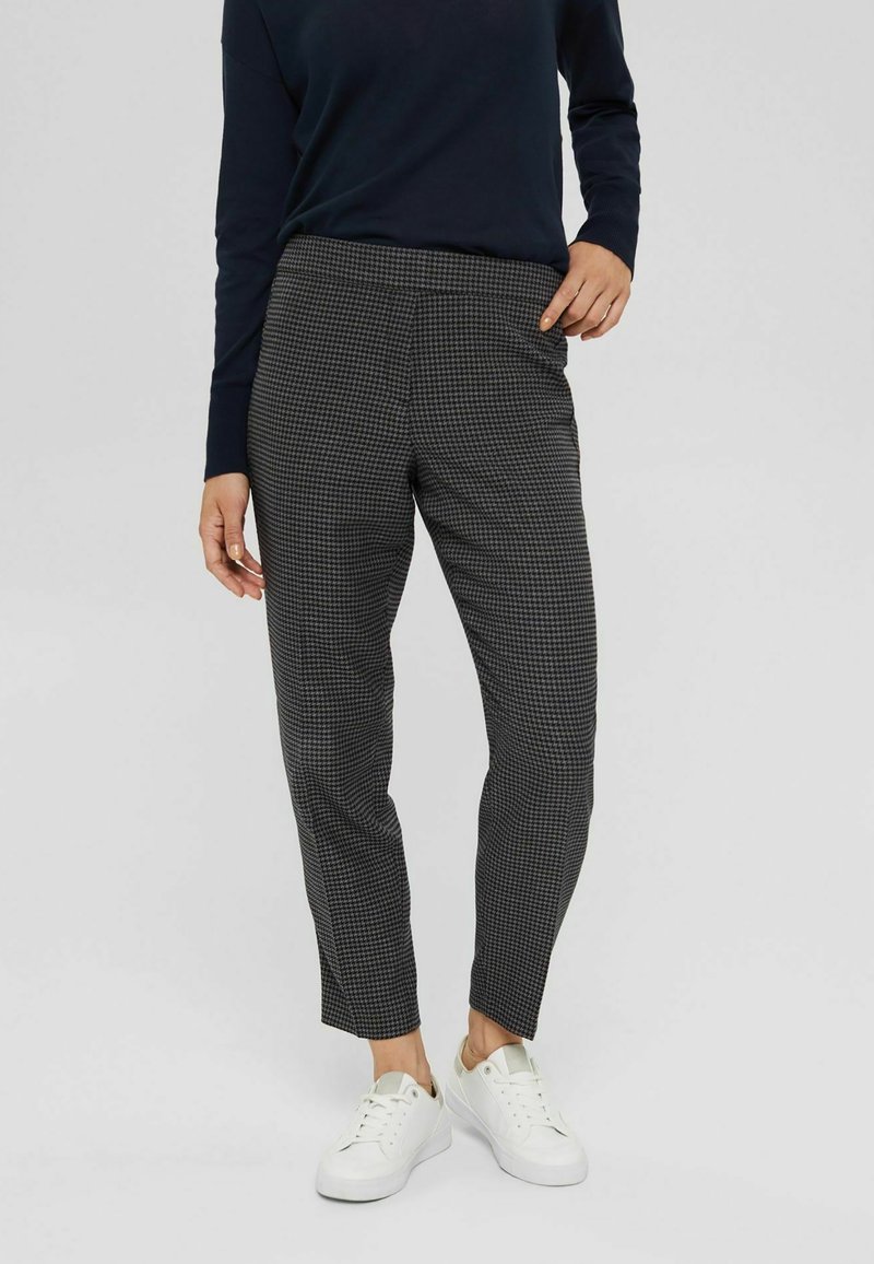 Pantalones a cuadros en blanco y negro con un corte ajustado, pernera tapered, cintura elástica y bolsillos laterales, combinados con zapatillas blancas.