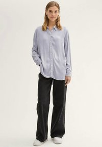 Šviesiai mėlyna marškiniai su ilgomis rankovėmis, lygiu audiniu, derinami su juodomis platėjančiomis kelnėmis ir baltais sportbačiais.