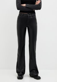 Pantalons évasés en cuir synthétique noir avec une fermeture éclair à l'avant, des poches et un léger éclat. Texture lisse avec des coutures contrastantes et une taille cintrée.