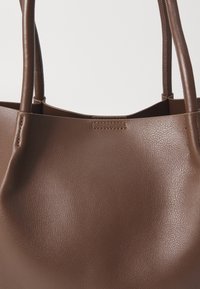 Sac cabas en cuir marron avec une texture lisse et des double poignées arrondies sur un fond clair uni.