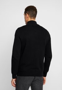 Maglione nero a maglia con colletto alto, polsini e orlo a coste. Il tessuto ha un aspetto texture, mostrando un design classico.