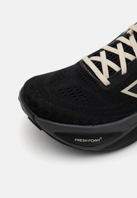 Chaussure de sport noire avec une tige texturée et des lacets de couleur claire. Dispose d'une semelle rembourrée avec la marque "FRESH FOAM" sur le côté.