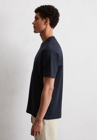 Granatowa bawełniana koszulka z okrągłym dekoltem, krótkimi rękawami i luźnym krojem. Gładka faktura, prosty design, bez widocznych wzorów czy akcentów.