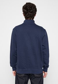 Felpa a collo alto di colore blu navy realizzata in un tessuto morbido, con orlo a costine. Texture liscia con dettagli di design minimi.