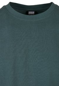 T-shirt à col rond bleu sarcelle en coton doux et léger. Présente un col côtelé et une texture lisse et unie sur toute la surface.