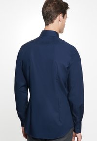 Donkerblauwe long-sleeve shirt met een klassieke kraag, gemaakt van gladde stof. Heeft knoopmanchetten en een gebogen zoom met zijsplitten.