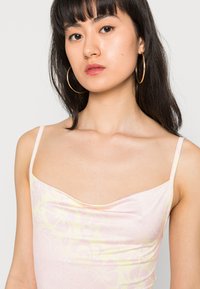 Top de alças cor-de-rosa claro com padrão floral amarelo, apresentando alças finas e decote drapeado, feito de um tecido liso e elástico.