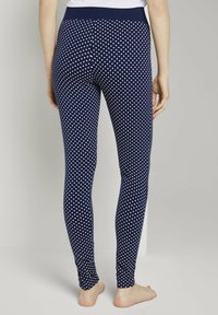 Marineblauwe leggings met witte polka dots, voorzien van een brede tailleband, rekbare stof en een gladde textuur, ontworpen voor comfort en pasvorm.