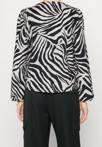 Haut à manches longues avec un motif rayé zèbre noir et crème, doté d'un col rond et de manches légèrement froncées, fabriqué en tissu doux.