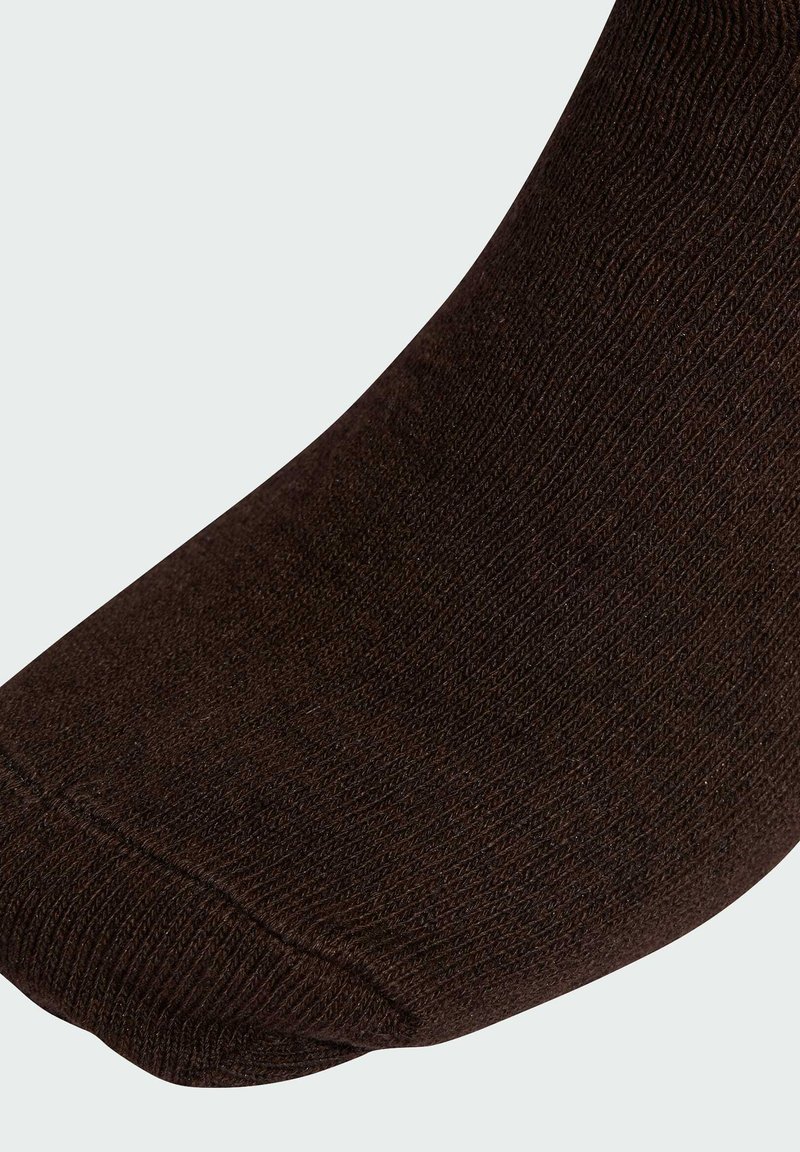 Brun strumpa med ribbad textur, rundad tå och sömlös design vid mudden. Materialet verkar mjukt och stickat.