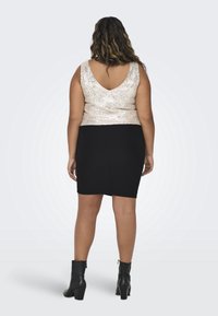 Svart åtsittande kjol i kombination med en guldglittrande linne. Linne har en V-ryggdesign, och modellen bär svarta ankelboots.