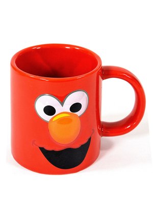 Tazza in ceramica rossa con un volto da cartone animato, occhi bianchi grandi, naso arancione e un sorriso nero. Forma arrotondata con un manico robusto.