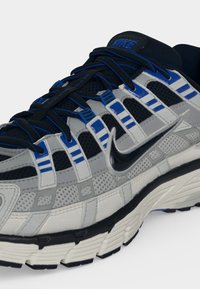 Αθλητικό παπούτσι Nike σε γκρι, μαύρο και μπλε με λεπτομέρειες από δίχτυ, χοντρή σόλα και μαύρο λογότυπο Swoosh στο πλάι.