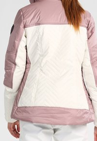 Veste à blocs de couleurs avec une partie supérieure rose clair et une partie inférieure crème, présentant un matelassage en chevrons et une silhouette ajustée.