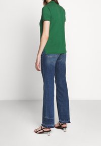 Grön poloshirt med krage, kombinerad med blå utsvängda jeans och svarta remsandaler. Skjortan har sidofickor i fållen.