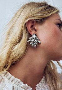 Sparkling silver earrings featuring a floral design with multiple marquise-shaped clear stones. Elaborate detailing and a textured backing.