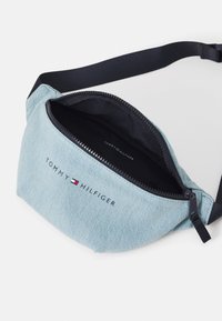 Šviesiai mėlynas džinsinis šlaunų krepšys su juodu reguliuojamu dirželiu ir užtrauktuku. Priekyje yra juodas "TOMMY HILFIGER" logotipas. Vidus tamsus.