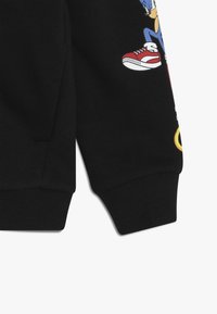 Svart linne med ribbade ärmar, med en färgglad Sonic the Hedgehog grafik och röda sneakers. Slät textur och avslappnad passform.