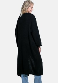 Długi czarny kardigan o luźnym kroju, teksturowanym dzianinie, z bocznymi rozcięciami i szerokimi rękawami, w połączeniu z jasnoniebieskimi dżinsami.