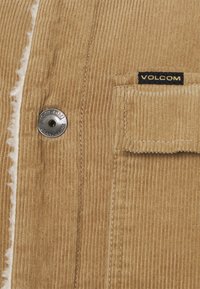 Jasnoszara kurtka z kordurojowej tkaniny z pionowymi prążkami, z metalowym guzikiem z logo "VOLCOM" oraz kieszonką naszywaną. Miękka w dotyku.