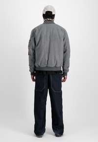 Siva fleece bomber jakna s rebrastim manžetama i donjim rubom, uparen sa tamnim traper širokim hlačama s džepovima od flisa.
