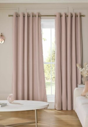 Tende rosa chiaro parzialmente aperte in un soggiorno con un tavolo rotondo bianco, vaso, divano beige e composizione di fiori secchi vicino a una finestra.
